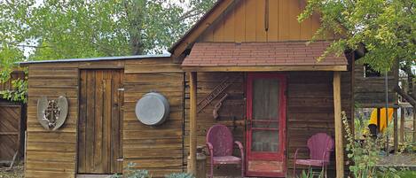 A wooden cabin with a porch, two chairs, and a small garden area.