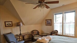 A bedroom with a large bed, two chairs, a table, a ceiling fan, and two windows. - Baxter Manor Spring City (Spring City)