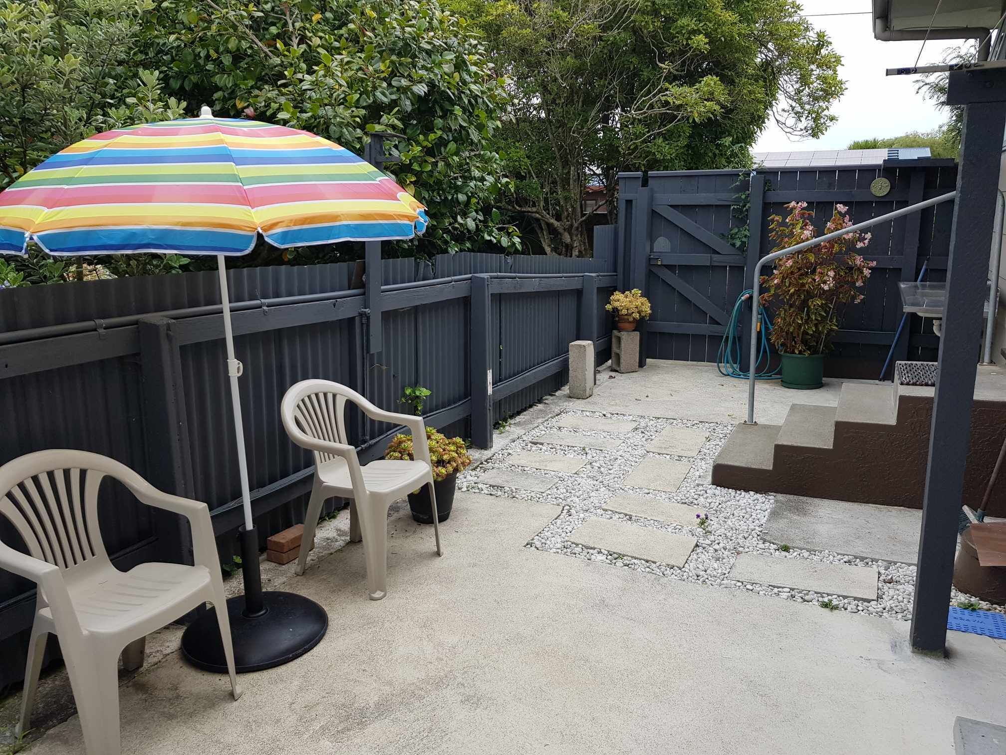 A patio area with a striped umbrella, two plastic chairs, and potted plants.