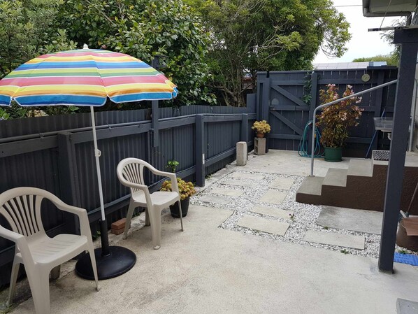 A patio area with a striped umbrella, two plastic chairs, and potted plants. - One on Vogel. (Woodville)