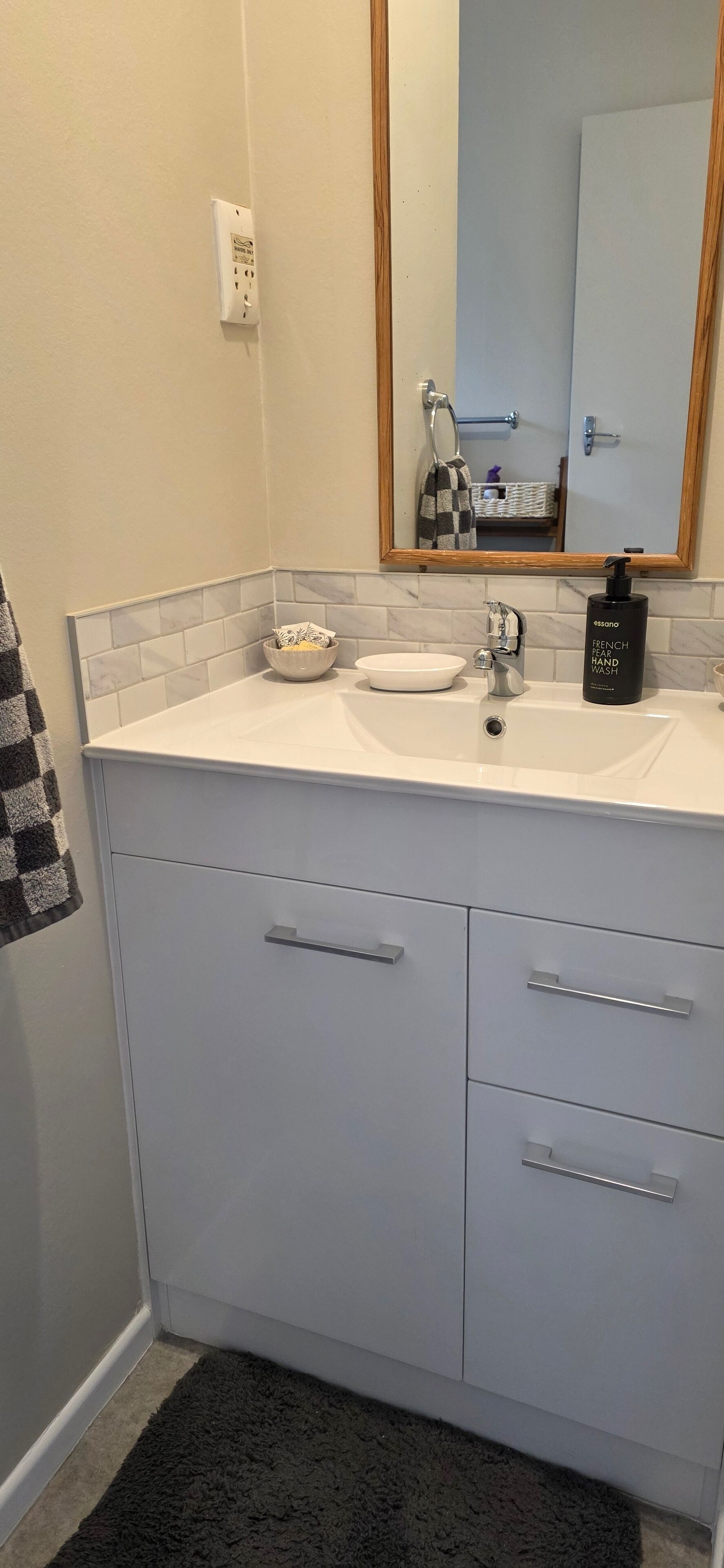 A bathroom with a white sink, a mirror, and a bottle of French Pear Hand Wash.