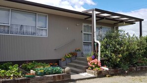 A single-story house with a covered porch, a small front yard with various potted plants, and a visible number '1' on the wall.