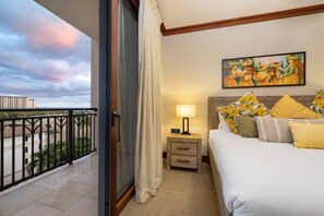 Une chambre d’hôtel avec un balcon, un lit avec une literie jaune et blanche, une table de chevet avec une lampe et un tableau au mur.