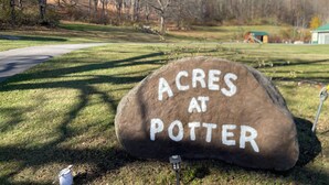 A large rock with "ACRES AT POTTER" written on it, surrounded by grass and trees. - Charming 2-bedroom country home in Middlesex / Potter (Middlesex)