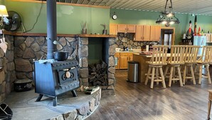 A rustic kitchen with a stone fireplace, wooden cabinets, and a bar area with stools. - Charming 2-bedroom country home in Middlesex / Potter (Middlesex)