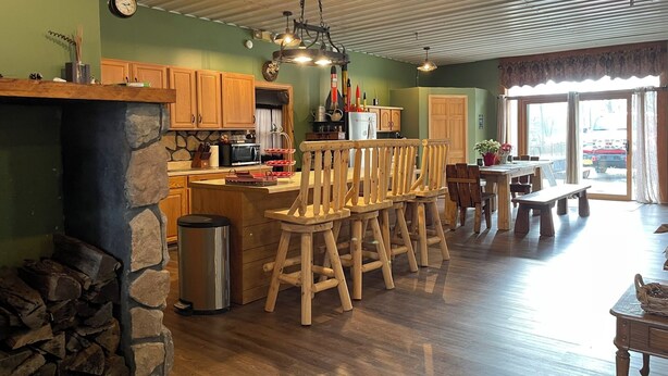 A spacious kitchen with wooden cabinets, a stone fireplace, and a large island with bar stools. - Charming 2-bedroom country home in Middlesex / Potter (Middlesex)