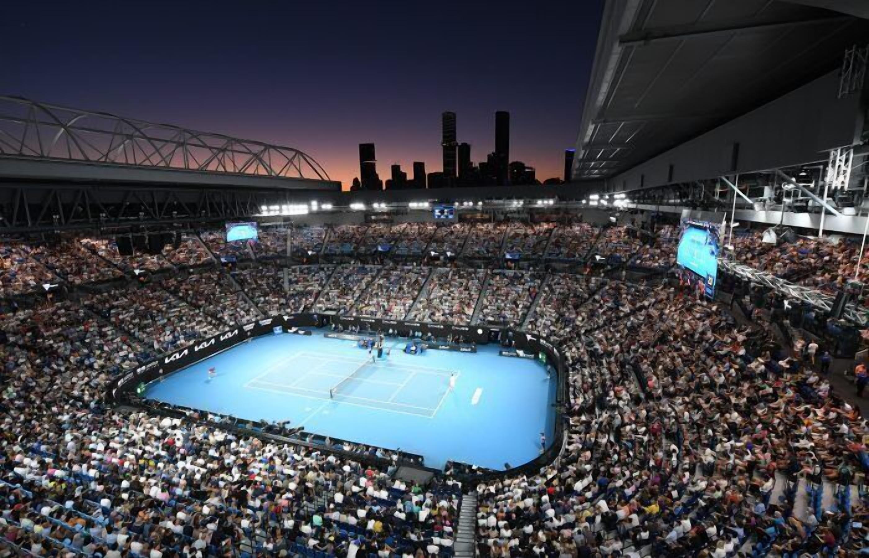 Een grote overdekte arena met een tennisbaan, omringd door een menigte toeschouwers.