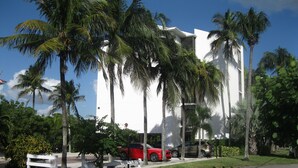 Un edificio moderno con fachada blanca, rodeado de palmeras y un coche rojo estacionado al frente.