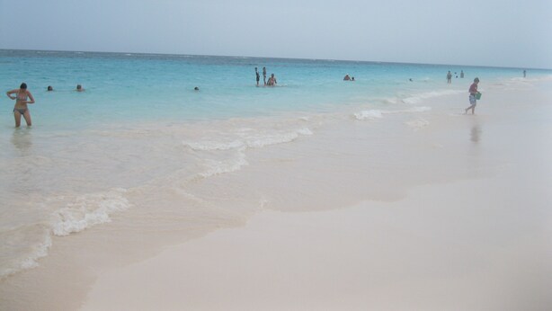 Una playa con gente nadando y caminando por la orilla.