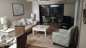 Una sala de estar con un sofá, una mesa de centro, un sillón estampado y una mesa de vidrio con una lámpara.