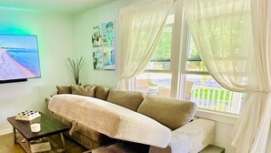 A modern living room with a beige sectional sofa, a coffee table, and a flat-screen TV mounted on the wall. - Charming 2-bedroom cottage steps away from the beach, restaurants, and downtown  (Port Austin)