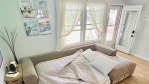 A bedroom with a large bed, a nightstand with a lamp, and a window with curtains. - Charming 2-bedroom cottage steps away from the beach, restaurants, and downtown  (Port Austin)