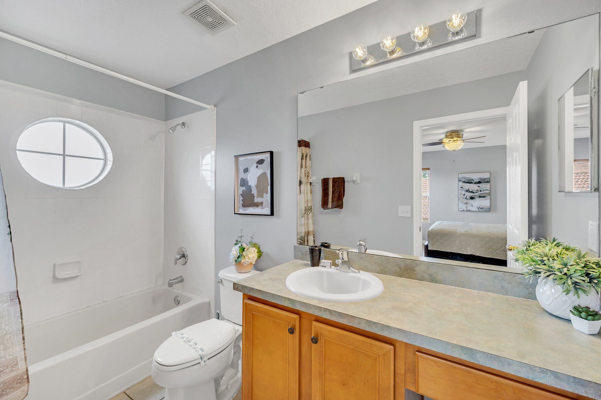 A bathroom with a bathtub, toilet, vanity with a sink, and a large mirror.