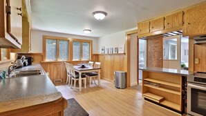 A kitchen with wooden cabinets, a stainless steel sink, a dining table with chairs, and a built-in oven.