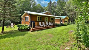 A wooden cabin with a porch and outdoor seating area surrounded by lush greenery.