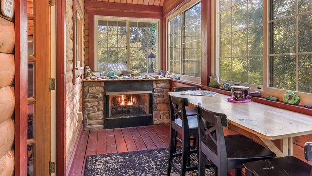 L’intérieur chaleureux d’un chalet avec une cheminée en pierre, des murs en bois et une grande fenêtre donnant sur la forêt.