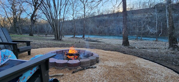 Relax by the fire pit in a serene outdoor setting surrounded by trees and a tranquil body of water.