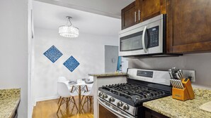A kitchen with a gas stove, stainless steel microwave, and granite countertops. There is a dining area with a white table and chairs. - Walk to Shands - 2nd Floor Condo (Gainesville)