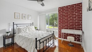 A bedroom with a bed, nightstand, lamp, and a white desk with drawers. - Walk to Shands - 2nd Floor Condo (Gainesville)