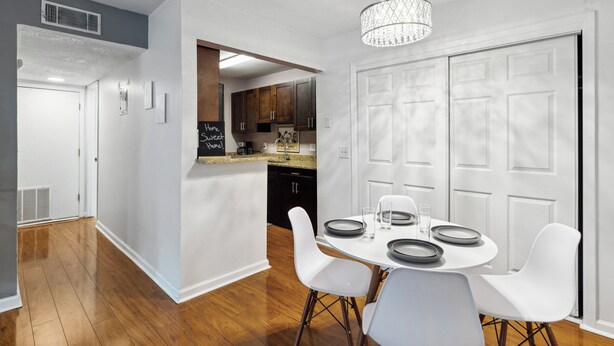 A modern kitchen with white cabinets, a granite countertop, and a dining area with white chairs and a round table. - Walk to Shands - 2nd Floor Condo (Gainesville)