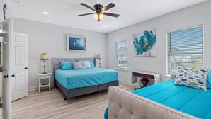 A bedroom with a bed, a ceiling fan, a nightstand, and a window with blinds. - Coco Cabana (Hackberry)