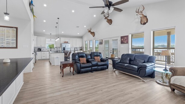 A spacious living area with a kitchen in the background, a ceiling fan, and mounted deer heads. - Coco Cabana (Hackberry)