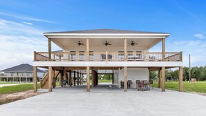 A two-story building with a covered patio area, outdoor seating, and a view of a house in the background. - Coco Cabana (Hackberry)