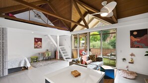 Een ruime woonkamer met een hoge plafond, een trap, een bank, een salontafel en grote ramen met uitzicht op het omliggende landschap.