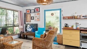 Ein modernes Wohnzimmer mit Korbmöbeln, einem Fernseher und einer Küchenzeile mit Schränken und Arbeitsplatte.