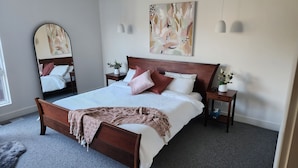 A neatly arranged bedroom with a wooden bed, a bedside table with a remote, and a mirror on the wall. - Luxury Coastal Townhouse Mornington (Mornington)
