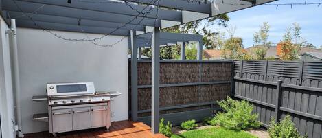 A patio with a built-in grill, a wooden deck, and a small lawn area.