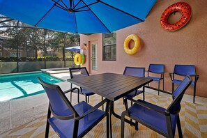 Une terrasse extérieure avec une piscine, des chaises bleues, une table et deux bouées gonflables accrochées au mur.