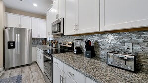 A modern kitchen with white cabinets, stainless steel appliances, granite countertops, and a backsplash with a mosaic tile pattern. - Experience Solterra: Pool, Spa, Game Room & Lazy River (Davenport)