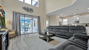 A spacious living room with a large grey sectional sofa, a modern coffee table, and a dining area with a chandelier. - Experience Solterra: Pool, Spa, Game Room & Lazy River (Davenport)