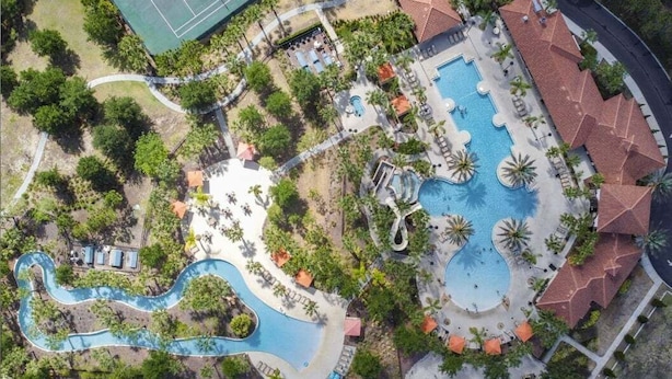 An aerial view of a resort with multiple swimming pools, palm trees, and lounge areas. - Experience Solterra: Pool, Spa, Game Room & Lazy River (Davenport)