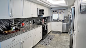 Una cocina moderna con armarios blancos, un microondas, un refrigerador de acero inoxidable y un salpicadero con diseño.