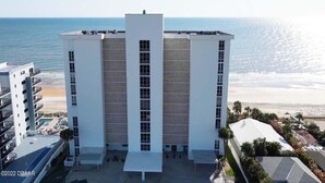 A modern hotel with a central tower, multiple balconies, and a view of the beach.