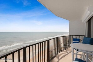 A balcony with a view of the ocean, a white table, and blue chairs. - Direct oceanfront in Ormond Beach Florida (Ormond Beach)