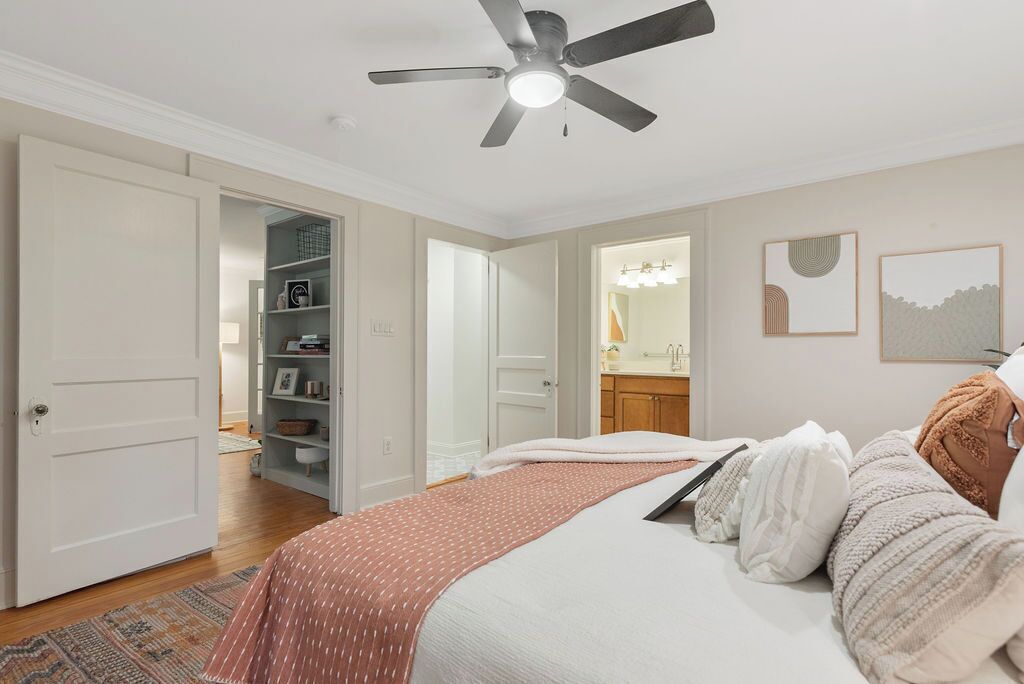 A bedroom with a bed, a ceiling fan, a wardrobe, and a bathroom visible through an open door.
