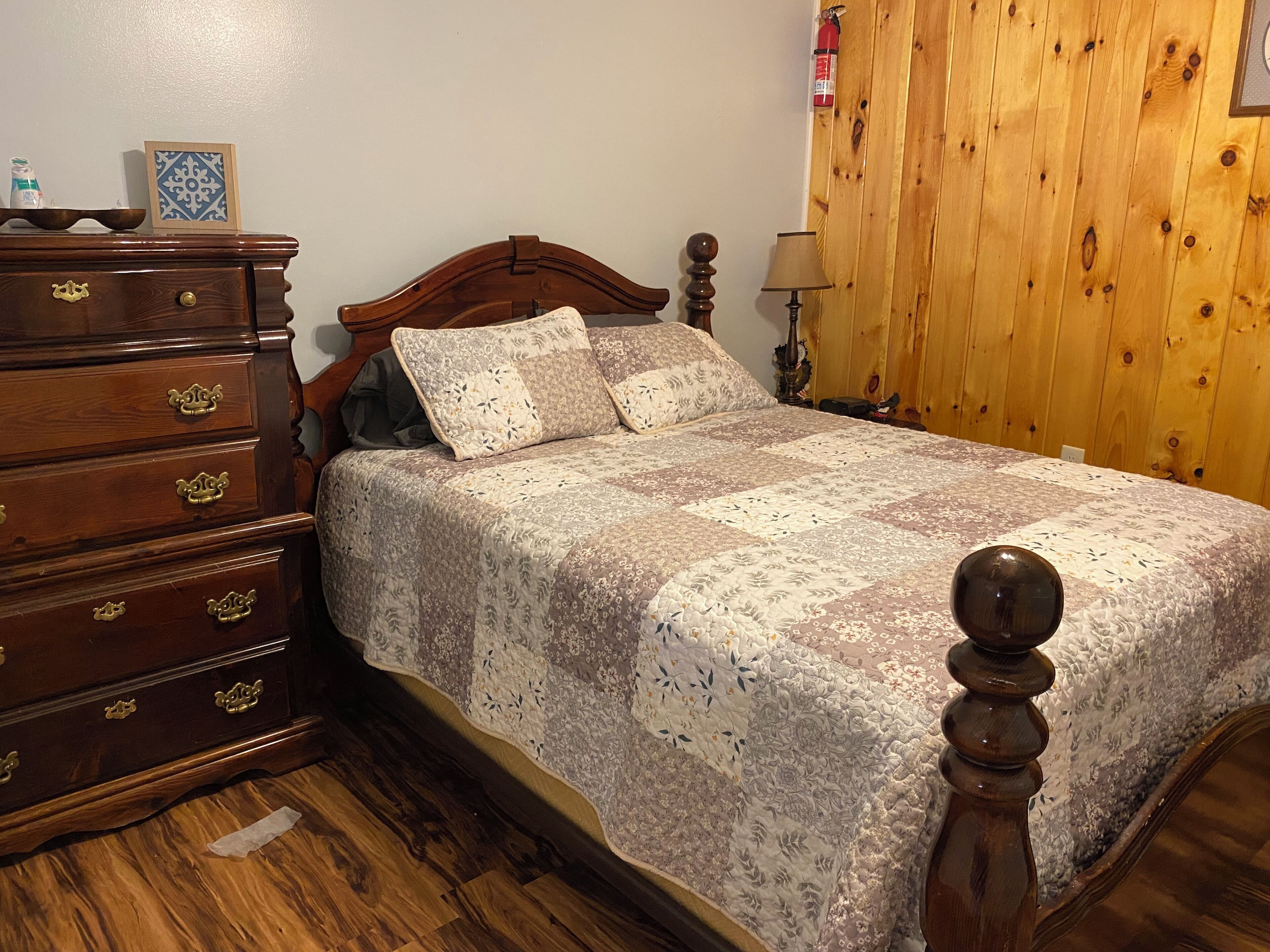Un lit en bois avec une courtepointe, une commode en bois avec des tiroirs et un panneau mural en bois.