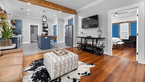 A spacious living room with a wooden ceiling, a large TV, and a dining area with a blue cabinet and a refrigerator.