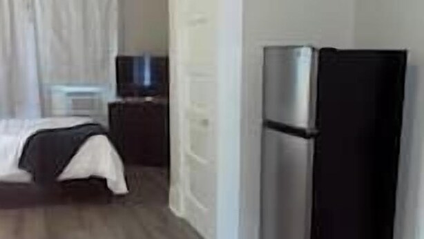 A room with a bed, a small table, a television, and a refrigerator. - Hideaway at Columbia (Shreveport)