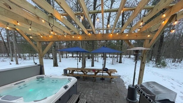 A covered outdoor area with a hot tub, picnic table, barbecue grill, and umbrellas. - Pine River Ranch-17 Acre Outdoor Paradise in the heart of the Manistee Forest (Wellston)