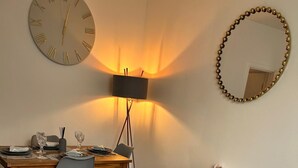 A neatly made bed with a white duvet and a grey throw, a grey chair, a wooden table with a lamp, and a round mirror on the wall. - Beautiful Abode in Brixton (London)