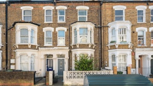A row of terraced houses with uniform brick facades, white-framed windows, and a central entrance gate. - Beautiful Abode in Brixton (London)