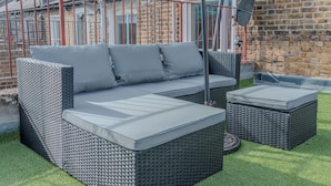 A wicker sofa with cushions and two ottomans in a garden setting. - Beautiful Abode in Brixton (London)