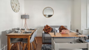 A modern living room with a dining area, a grey sofa, a wooden coffee table, and a round mirror with a gold frame. - Beautiful Abode in Brixton (London)