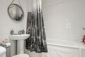 A bathroom with a white sink, mirror, and bathtub. - Beautiful Abode in Brixton (London)