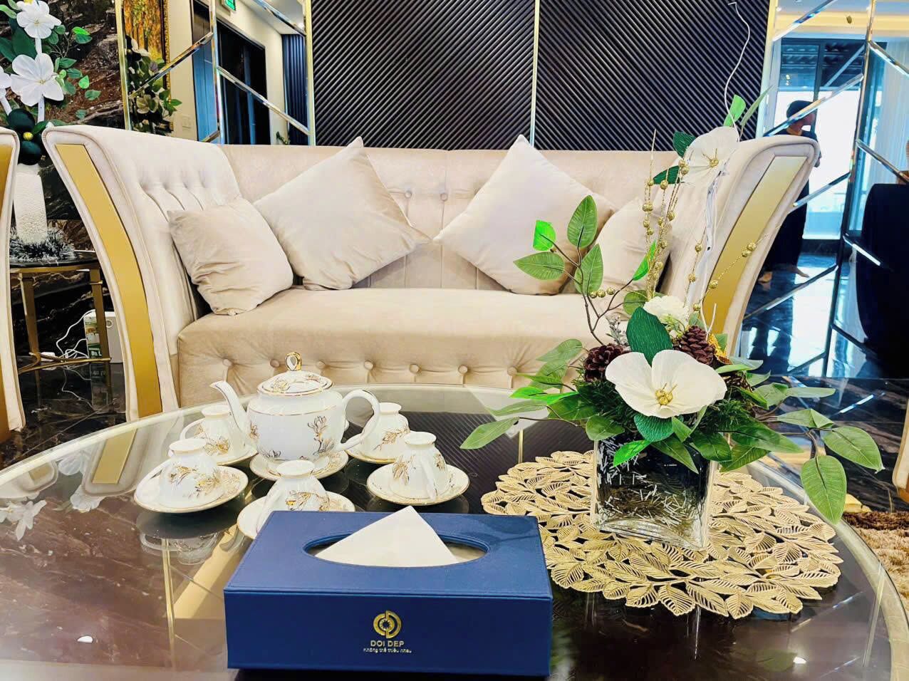 A room with a sofa, a table with tea set, and a vase with flowers.