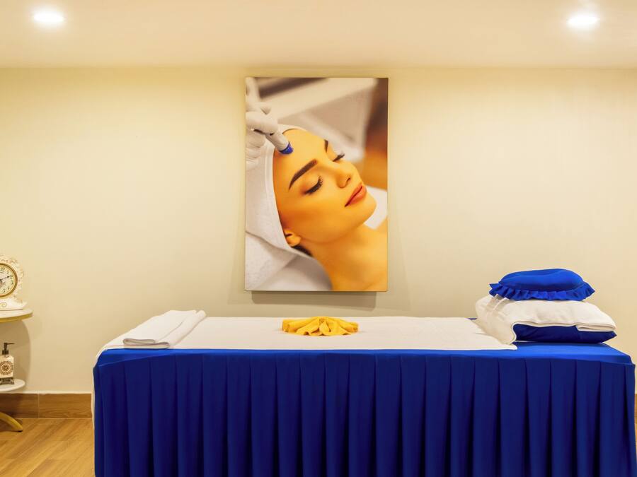 A room with a blue-covered massage table, a clock, and a vase of flowers on a side table.